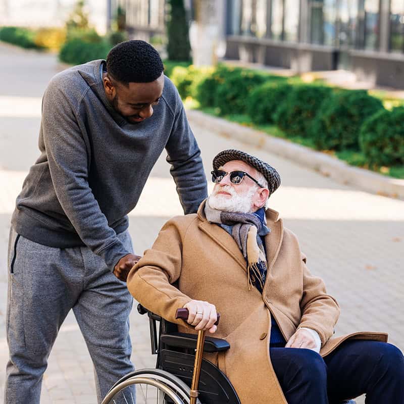 man helping older man in wheelchair cross the street